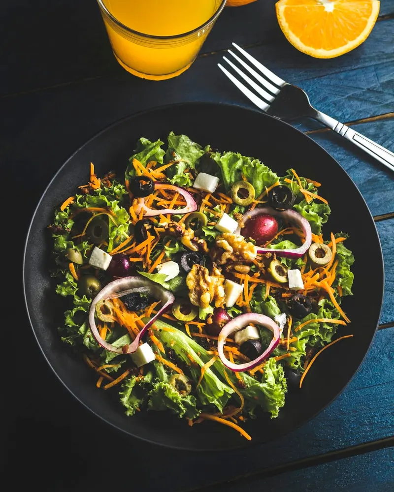 Ensalada con hojas verdes, cebolla morada, aceitunas y queso en plato negro