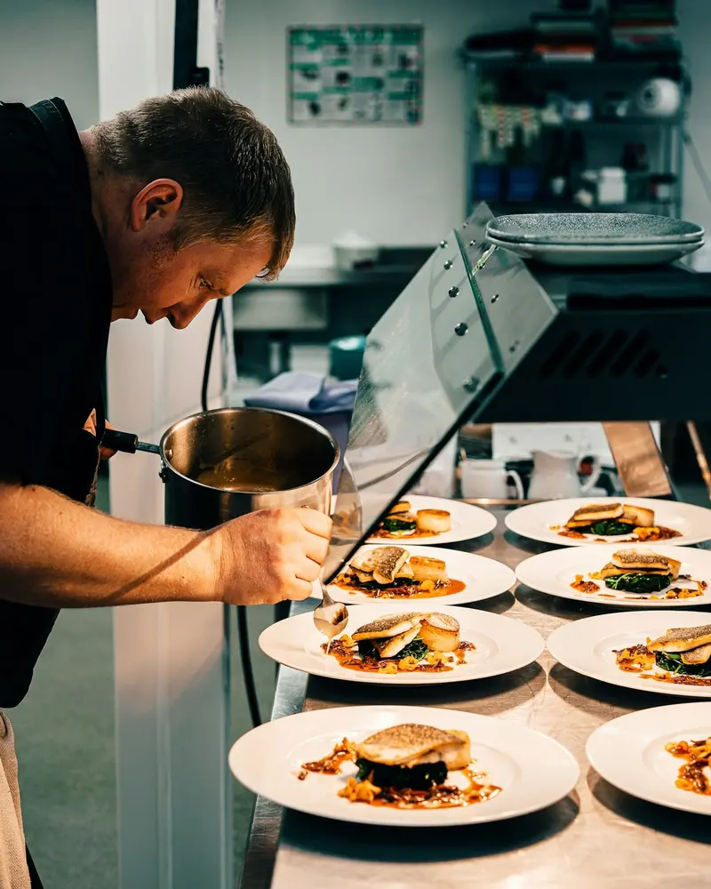 Cocinero terminando varios platos en el pase de la cocina