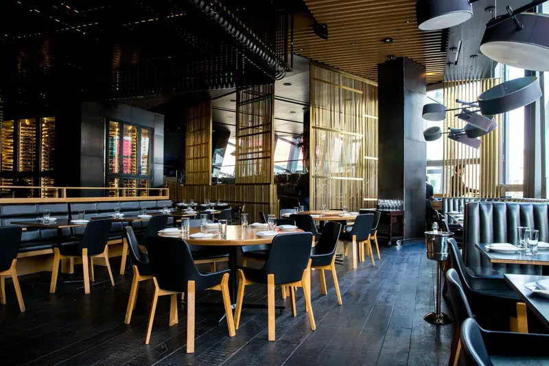 Salón con mesas de madera, sillas tapizadas e iluminación cálida