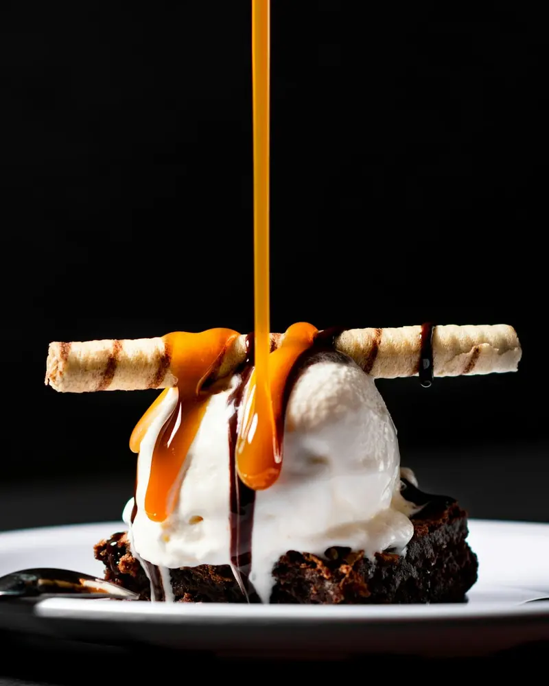 Helado con barquillo y caramelo derramándose sobre un brownie